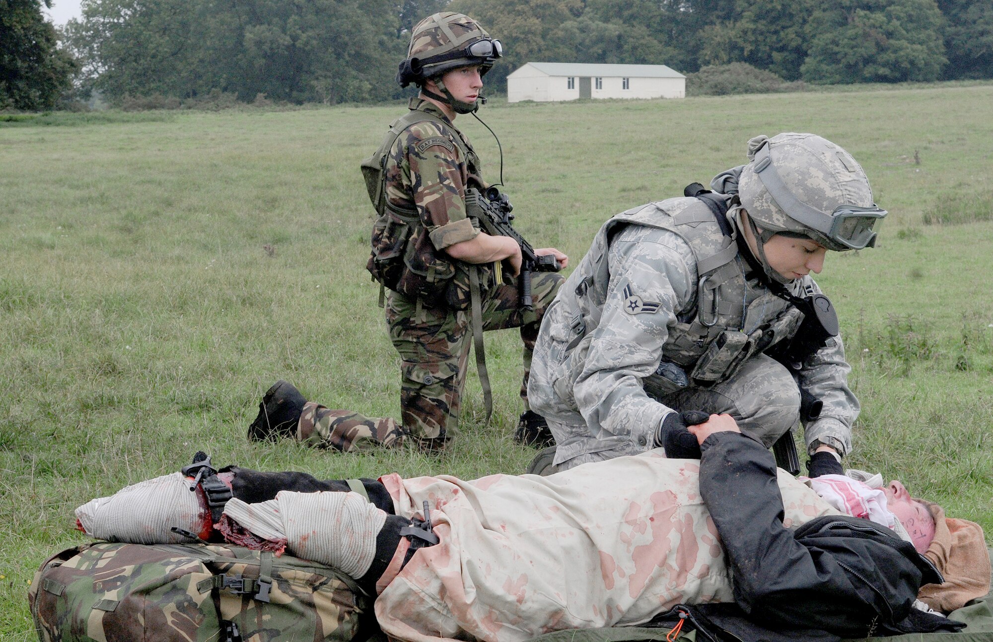 Airman 1st Class Ali Rickman (right) comforts a "patient" while a member of the Royal Air Force Regiment provides security as they await helicopter transport during a mass casualty training scenario Sept. 8, 2010, at Stanford Training Area, England. More than 20 Airmen embedded in training with the regiment to give the British servicemembers an idea of what it is like to work with United States forces. The regiment flight was conducting its last training scenarios before deploying to Afghanistan with U.S. Marines. Airman Rickman is assigned to the 100th Security Forces Squadron at Royal Air Force Mildenhall, England. (U.S. Air Force photo/Staff Sgt. Thomas Trower) 
