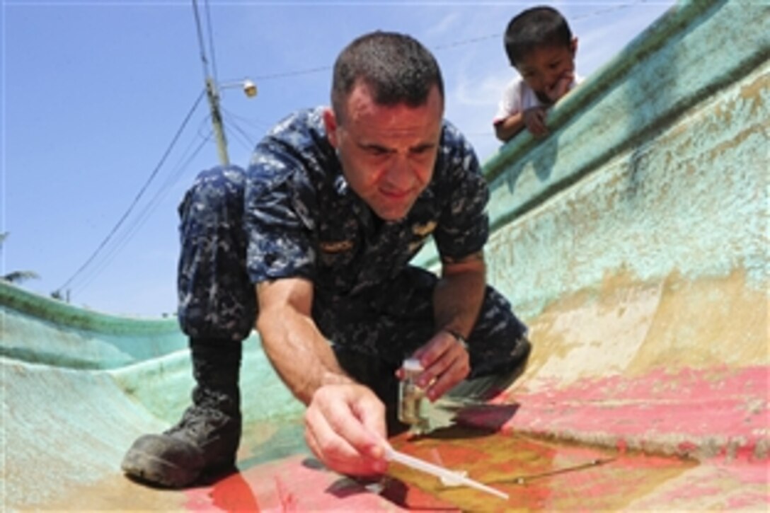 U.S. Navy Lt. Michael Kavanaugh  takes water samples as a Guatemalan boy watches in Puerto Barrios, Guatemala, Sept. 10, 2010. Kavanugh and other sailors aboard the USS Iwo Jima are participating in the Continuing Promise 2010 humanitarian civic assistance mission.