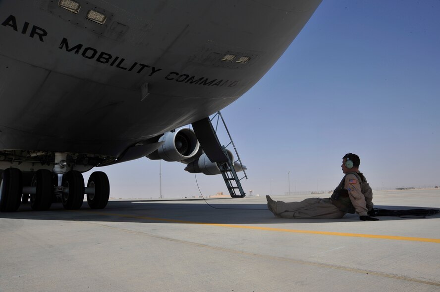 A flying crew chief relaxes under the giant shadow of a C-5 Galaxy away from the hot sun while he waits for engine start Sept. 13, 2010 at Al Asad Air Base, Iraq. The C-5 is moving vehicles and equipment no longer needed in Iraq, due to the drawdown, back to the U.S., or Afghanistan. (U.S. Air Force Photo/Senior Airman Perry Aston)