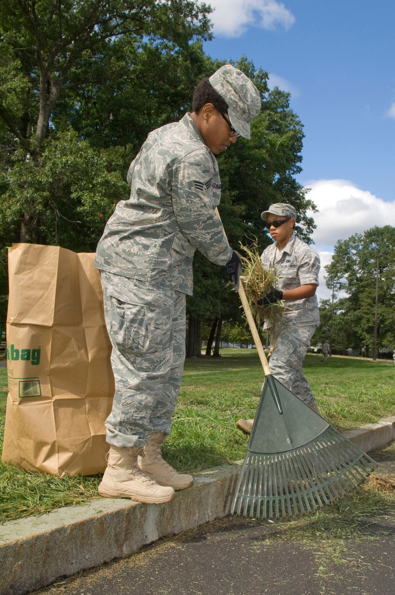 HANSCOM AIR FORCE BASE, Mass. – Senior Airman Raenatta Gammons (left), with the 66th Logistics Readiness Squadron, rakes-up grass on and Senior Airman Latrice Bullock picks up piles of grass along Marrett Street near Castle Park on Sept. 10.  Sixteen Airmen dedicated their day to mowing common areas around Hanscom to improve the overall base appearance. (U.S. Air Force photo by Mark Wyatt)