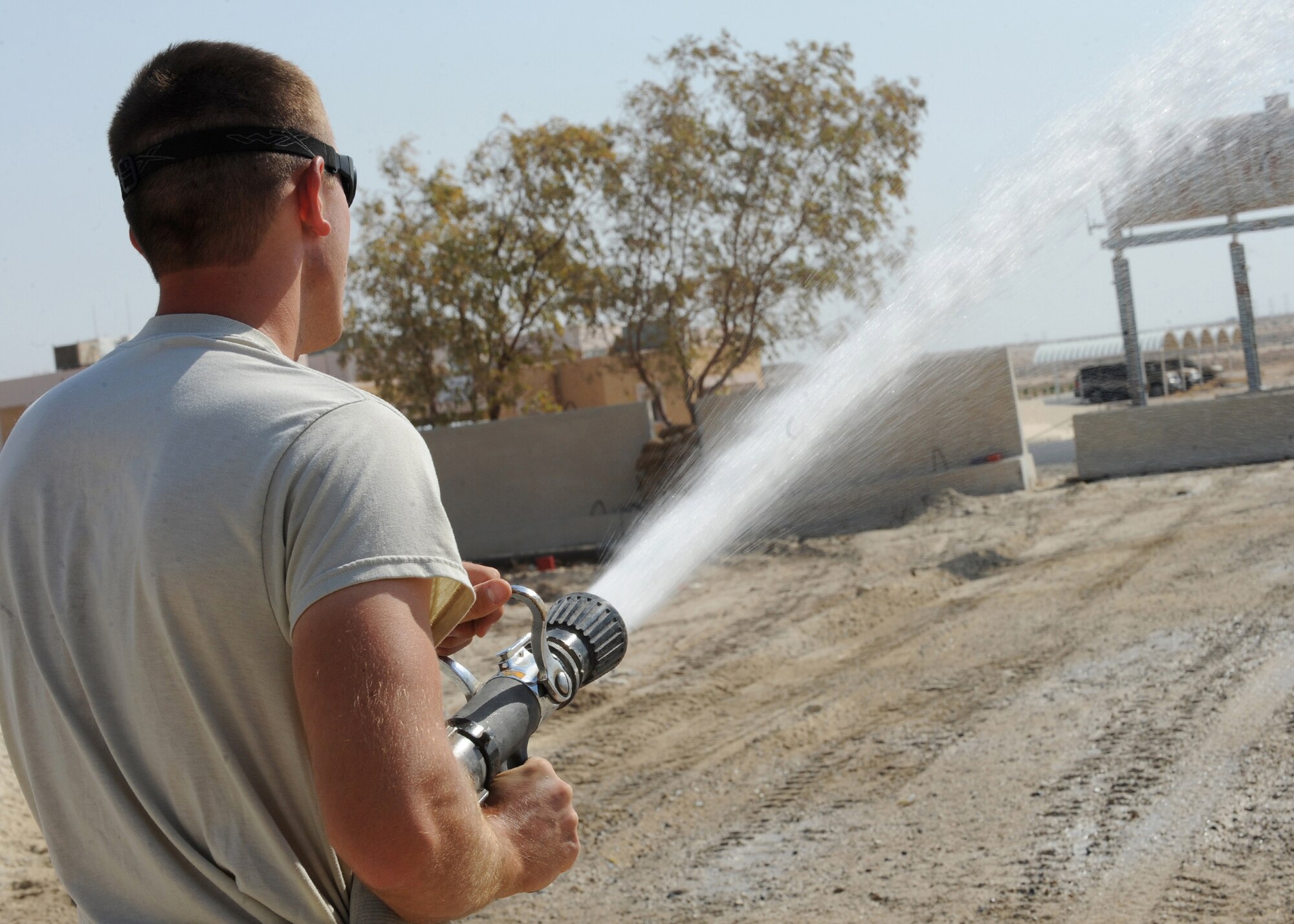 SOUTHWEST ASIA - Airman 1st Class John R. Sherill of the 386th Expeditionary Civil Engineer Squadron waters the sand with a hose from a water truck before laying down asphalt at an undisclosed location here Sept. 8, 2010. The sand needs water in order to stay packed when asphalt is applied. (U.S. Air Force photo by Senior Airman Laura Turner)