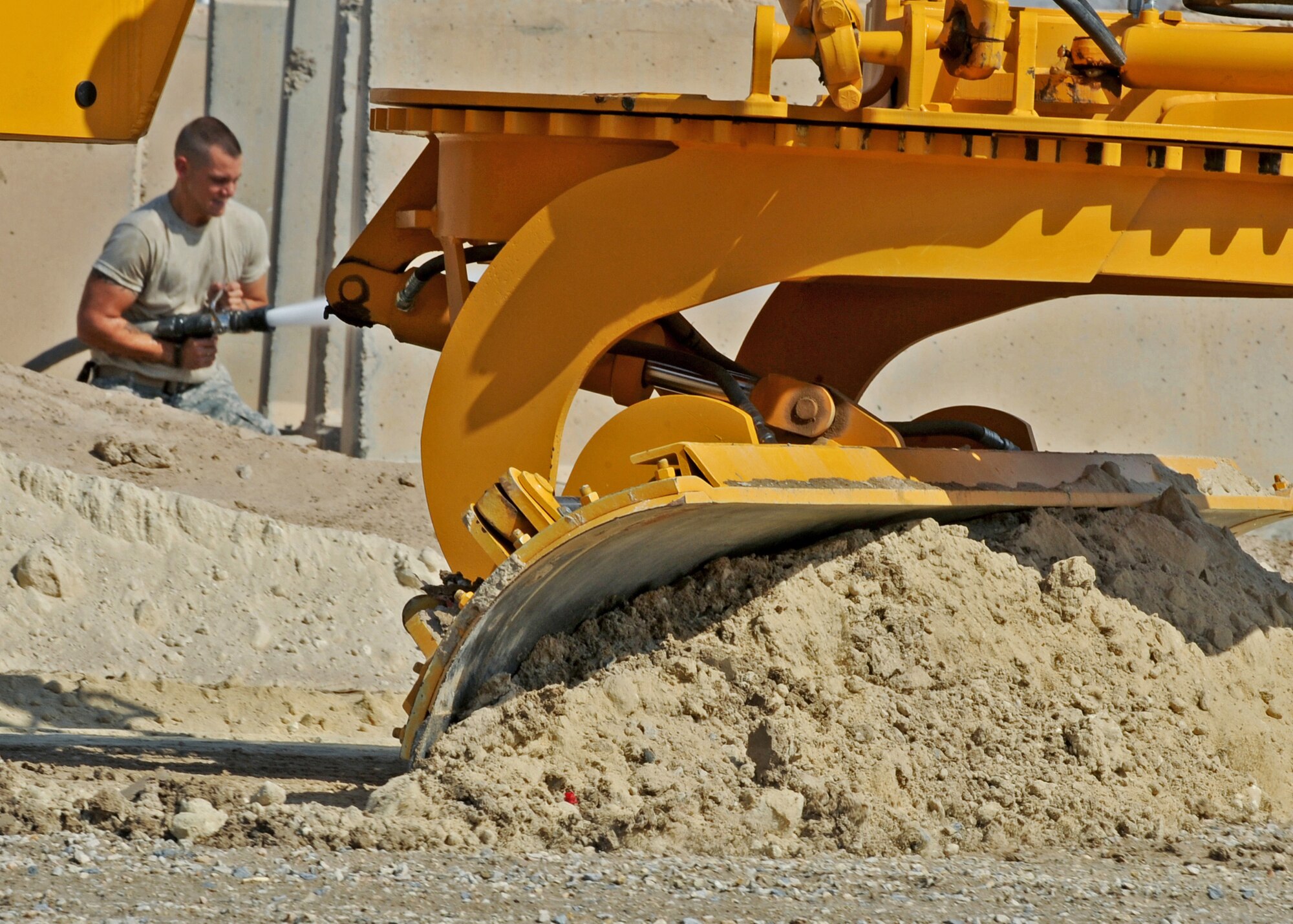SOUTHWEST ASIA - Senior Airman Jacob Cleer of the 386th Expeditionary Civil Engineer Squadron sprays the sandy ground with water while an excavator blade levels out dirt in preparation for asphalt to be applied at an undisclosed air base here Sept. 8, 2010. CE is responsible for facility maintenance, airfield paving, explosive ordinance disposal and environmental management. (U.S. Air Force photo by Senior Airman Laura Turner)