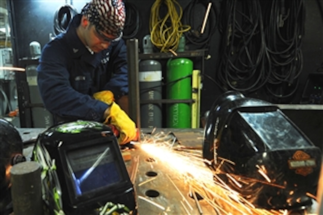 U.S. Navy Petty Officer 3rd Class Dustin Green removes weld splatters and other residue from the welding table in the repair shop aboard the aircraft carrier USS Harry S. Truman in the Arabian Sea, Sept. 15, 2010.