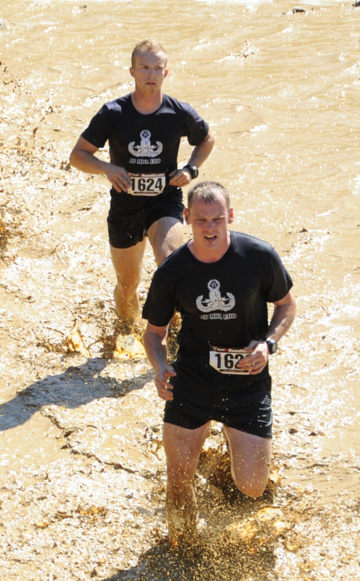 Two members of the Joint Base McGuire-Dix-Lakehurst Explosive Ordnance Disposal Team, run through a foot of muddy water on their way to the “Dragon Teeth” obstacle. (U.S. Air Force photos/Staff Sgt. Danielle Johnson)
