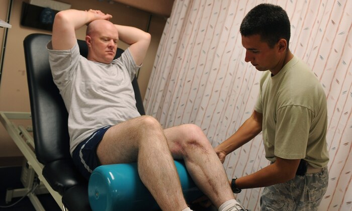 NELLIS AIR FORCE BASE, Nev.-- Senior Airman Joseph Suarez, 99th Medical Operation Squadron physical therapy journeyman, assists Master Sgt. Jeramie Brown, 99th Air Base Wing broadcast journalist, with an exercise known as short arc quads Sept 21. Airman Suarez works with Sergeant Brown bi-weekly to improve range of motion and strengthen his muscles. (U.S Air Force Photo / Senior Airman Stephanie Rubi)