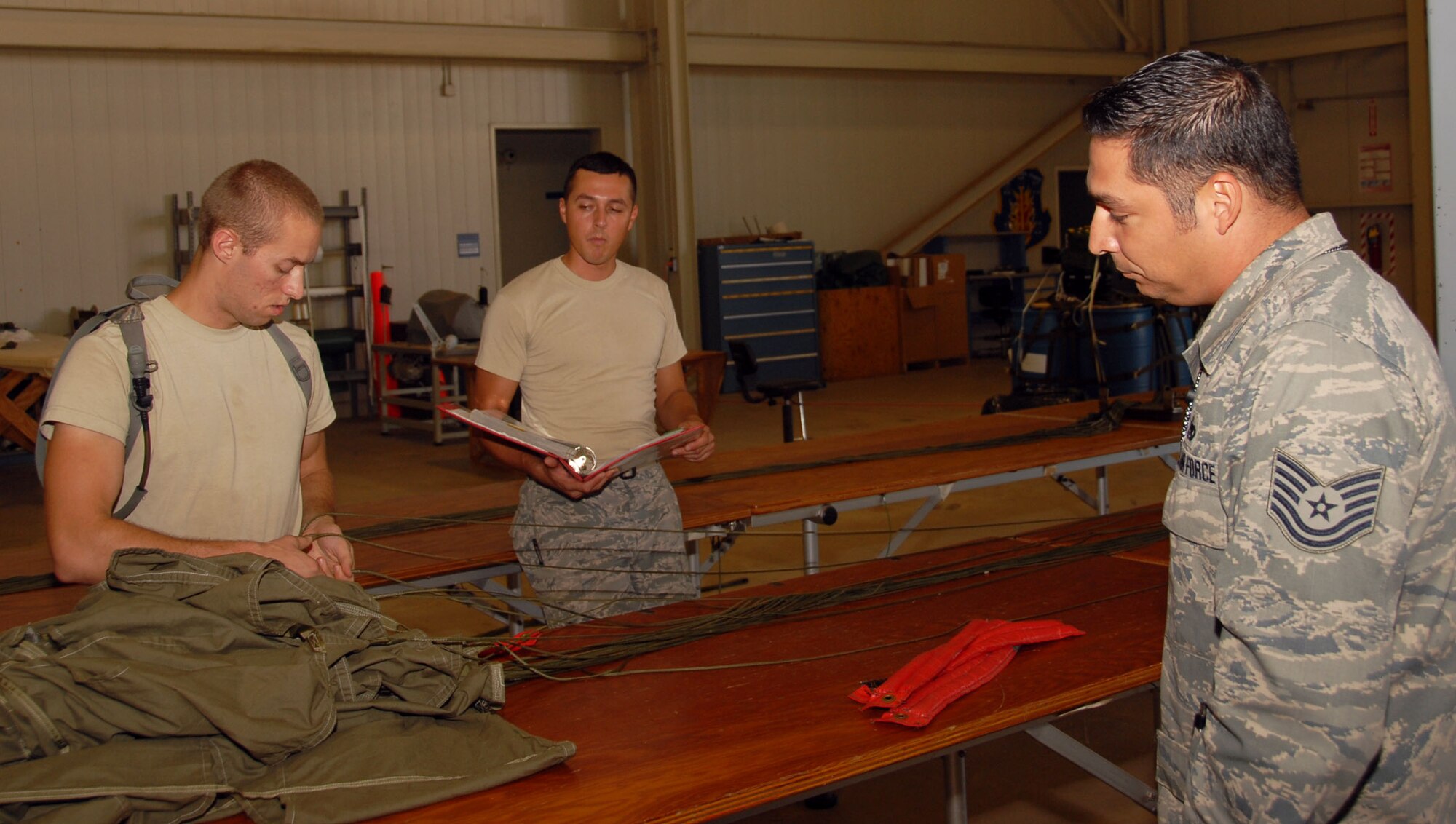 ALTUS AIR FORCE BASE, Okla. – (L to R) Airman 1st Class Adam Locke and Airman 1st class Angelo Llorente, from the 97th Logistics Readiness Squadron, work together doing a line check on a parachute during the Logistics Compliance Assessment Program inspection September 15. (R) Tech. Sgt. Cesar Valencia Air Education Training Command (LCAP) inspector watches to make sure they are doing it right. (U.S. Air Force photo by Airman 1st Class Christopher Arnold/Released 97th Air Mobility Wing – Public Affairs)