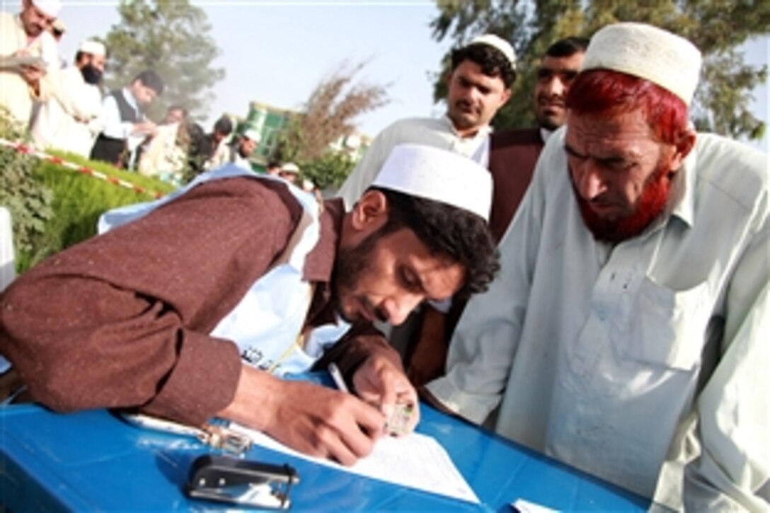 An Afghan worker verifies the identification card of a resident during parliamentary elections at a polling center in the Matun district, Khost province, Afghanistan, Sept. 18, 2010. 