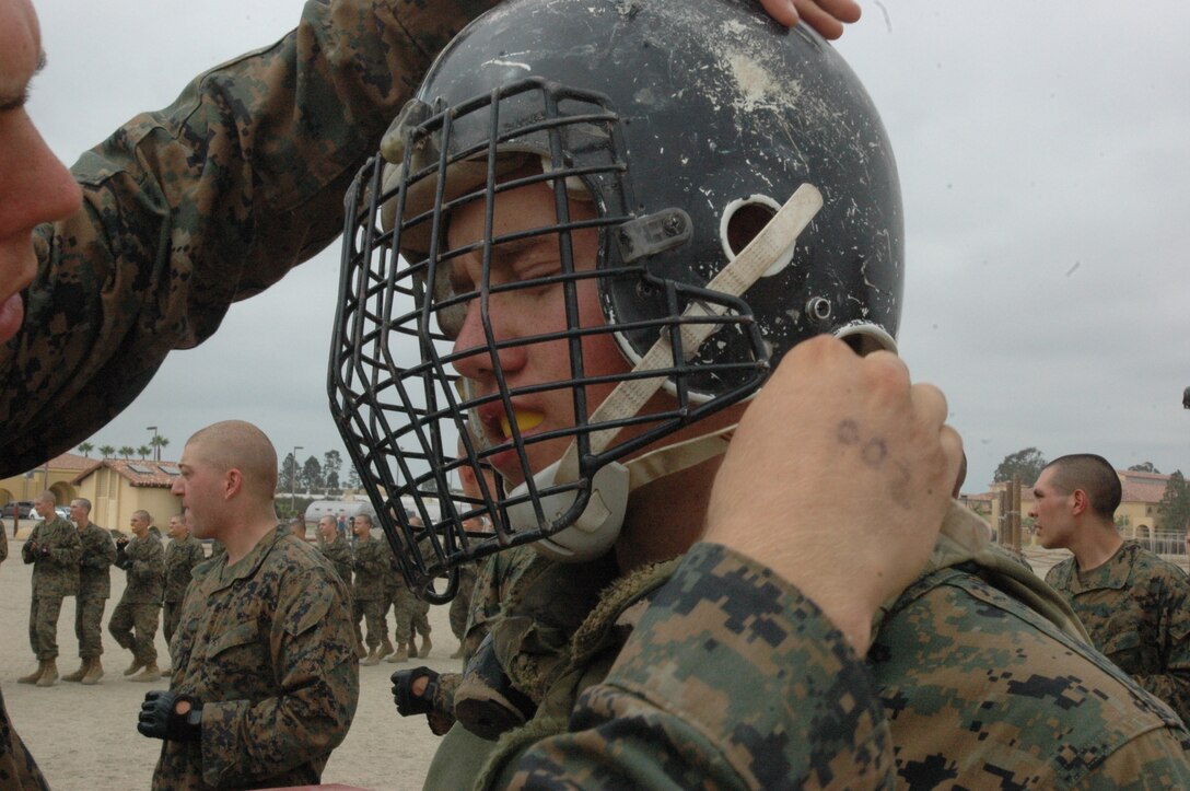Recruit Matthew Santoyo, Platoon 2108, Company E, 2nd Recruit Training Battalion, snaps the chin strap to the helmet that recruit Tyler West, Platoon 2108, Co. E. 2nd Recruit Training Bn. was wearing before his pugil sticks match here, Sept. 21.