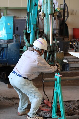 Masashi Muranaka, Japanese construction worker, attaches a line around one of the old in-ground hydraulic lifts and attaches it to a forklift during the construction of the new more efficient above-ground hydraulic lifts in the Marine Wing Support Squadron 171 motor transportation garage here Sept. 21. After removing the old in-ground lifts, the workers filled the space with concrete to install the new lifts.
