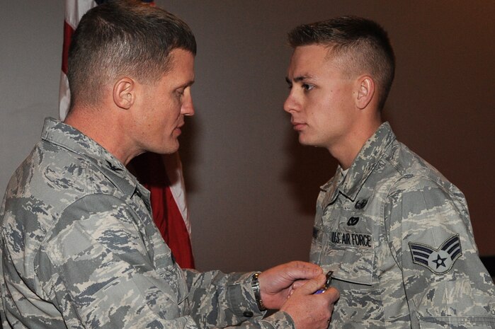 Retired Col. Dave Belote, former 99th Air Base Wing commander, presents the Purple Heart to Senior Airman Michael Buras, 99th Civil Engineer Squadron explosive ordnance disposal journeyman, at the Nellis Theater during a commander's call Dec. 4, 2009.  Airman Buras died Sept. 21 of wounds suffered as the result of an improvised explosive device detonation in Kandahar, Afghanistan. (U.S. Air Force photo by Lawrence Crespo)
