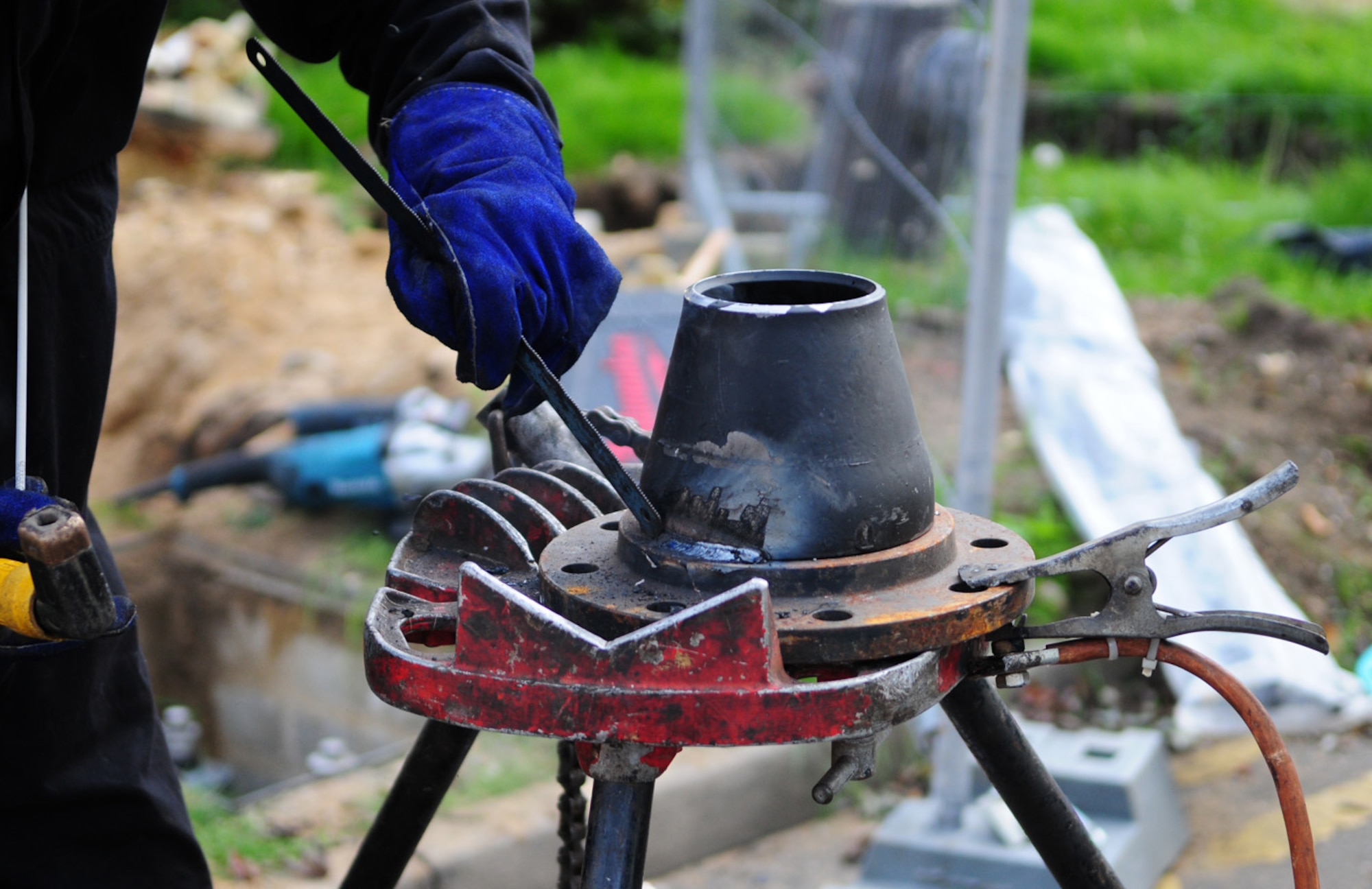 RAF MILDENHALL, England -- A contractor uses a serrated metal blade to chip off slag from a piece of steel, which will be linked to the district heating main and one of the boiler houses on base. The building it was originally linked to is being demolished. Once the slag is cleaned off, the metal will be welded to protect it from the elements. (U.S. Air Force photo/Karen Abeyasekere)