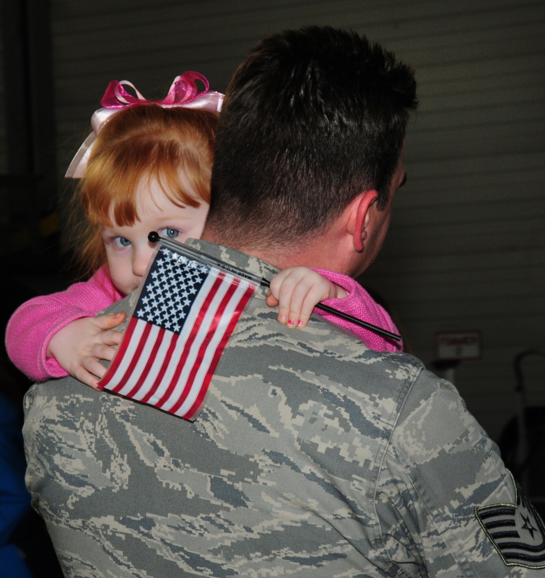 SPANGDAHLEM AIR BASE, Germany – Madison Mason peers over her father’s shoulder while clutching a small American flag during the 81st Fighter Squadron redeployment. Her father, Tech. Sgt. Cole Mason, 52nd Medical Support Squadron laboratory NCOIC, deployed to Afghanistan in 2009 and attended to support the return of his fellow servicemembers. (U.S. Air Force photo/Staff Sgt. Heather M. Norris)
