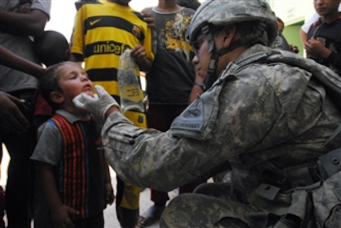 U.S. Army Spc. Nicholas Cisneros, a combat medic, with Headquarters and Headquarters Company, 1st Battalion, 37th Armor, 1st Brigade Combat Team, 1st Armored Division, out of Fort Bliss, Texas, provides medical aid to a young Iraqi boy before the ribbon cutting ceremony for Al Bassa Girls Primary School in the village of Tal Jal northwest of Hawijah, Iraq, on July 6, 2010.  
