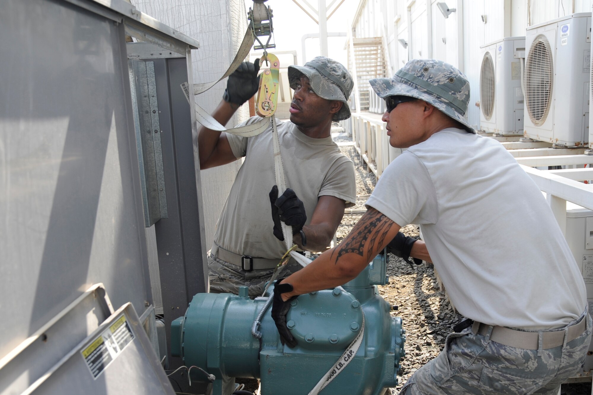 (Left to right) Airman 1st Class LeAndre Davis and Senior Airman Mathew Bright, 380th Expeditionary Civil Engineer Squadron heating ventilation and air conditioning technicians, guide an air conditioner compressor into place Sept. 23, 2010 at an undisclosed location in Southwest Asia. (U.S. Air Force photo/Tech. Sgt. April Wickes)