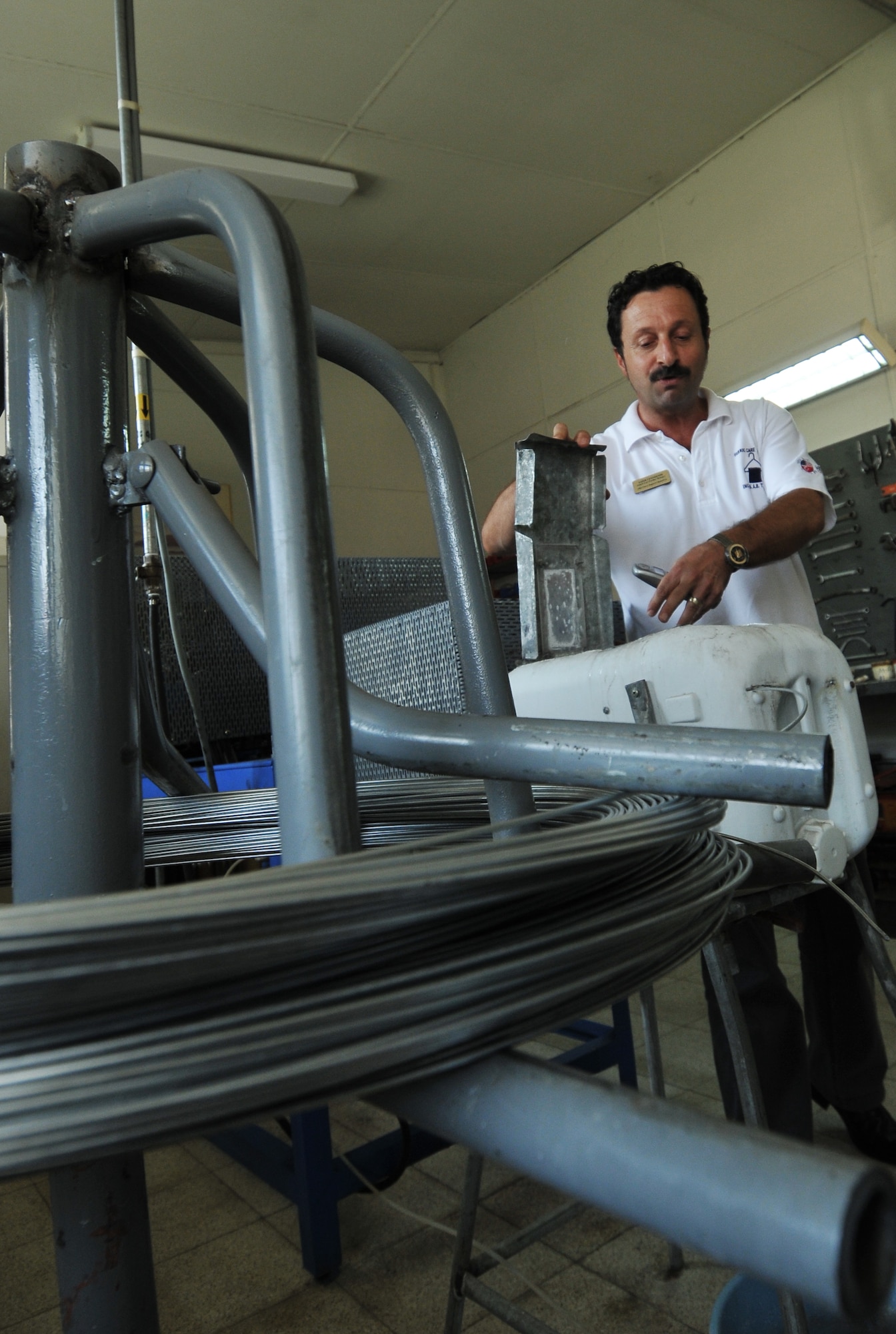 Zafar Cetindemir, Incirlik Fabric Care Facility manager, explains how a hanger-making machine functions Sept. 21, 2010 at Incirlik Air Base, Turkey. This machine was created by Bedir Tanir, Incirlik Fabric Care Facility mechanic using recycled parts and contributed to the $131,000 saved by the facility since 2000. (U.S. Air Force Photo/ Senior Airman Alexandre Montes)