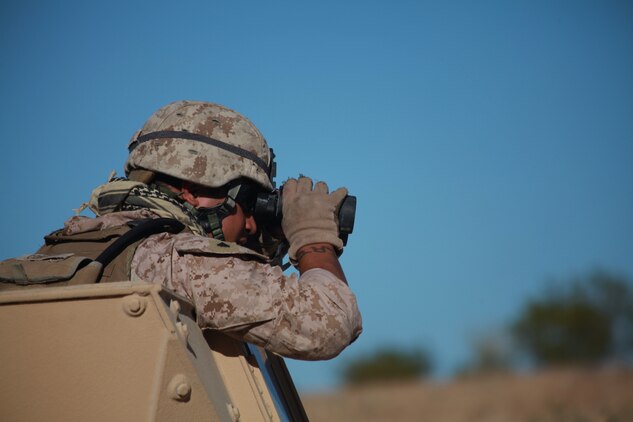 Corporal Maulalo Cortez, a rifleman from Company G, 2nd Battalion, 4th Marine Regiment, peers through his binoculars after engaging enemy targets Sept. 27 at Combat Center Range 220. The Combat Center’s Advisor Training Group trains Marines like Cortez to get them prepared to train Afghan forces. (Photo by: Lance Cpl. M. C. Nerl)::r::::n::