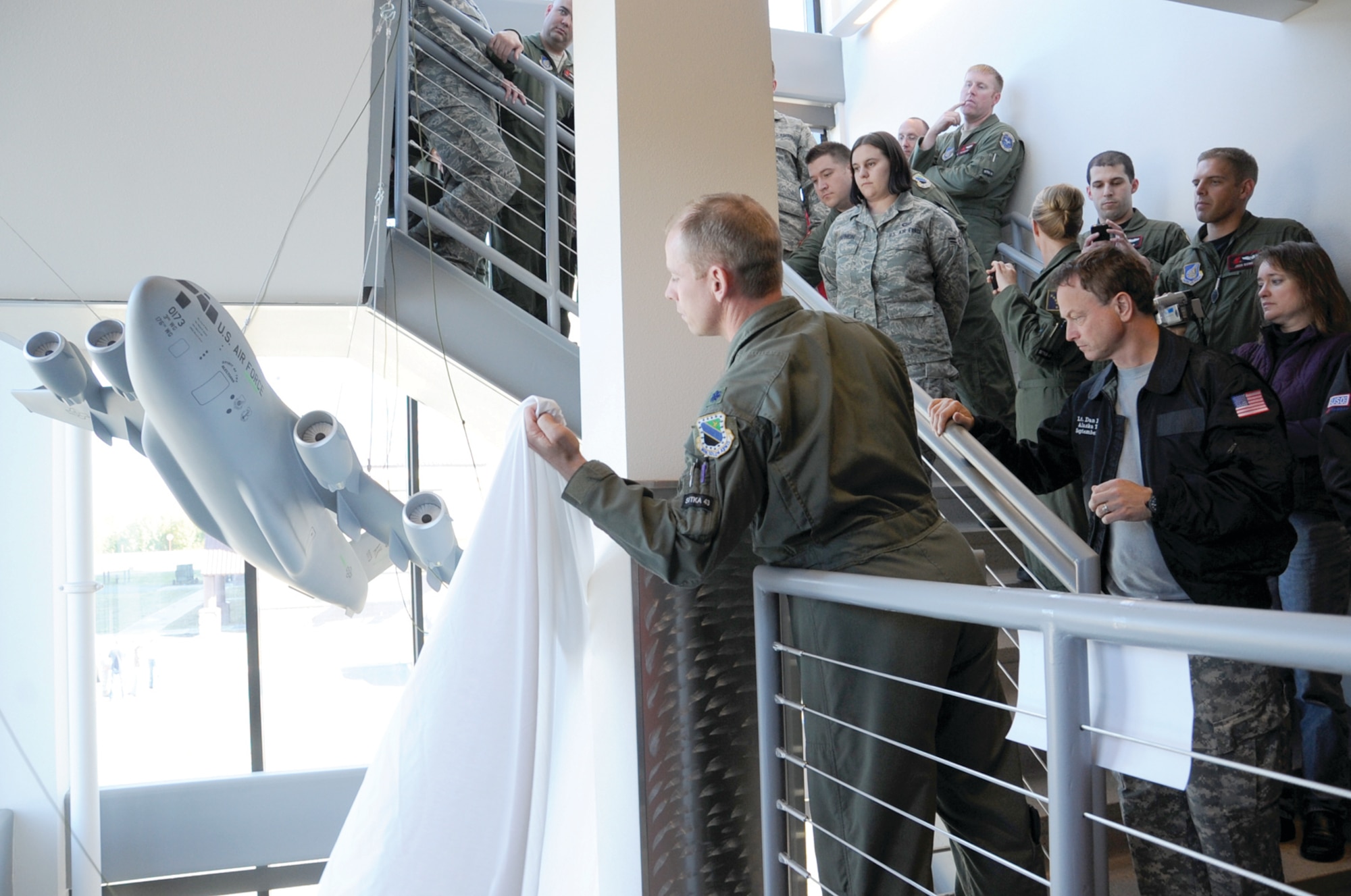 Air Force Lt. Col. Patrick Weeks, 517th Airlift Squadron commander, catches the veil which shrouded the Sitka 43 Memorial model after it was released by actor Gary Sinise, Sept. 16, at the squadron headquarters. (Photo by Senior Airman Cynthia Spalding/JBER PAO)