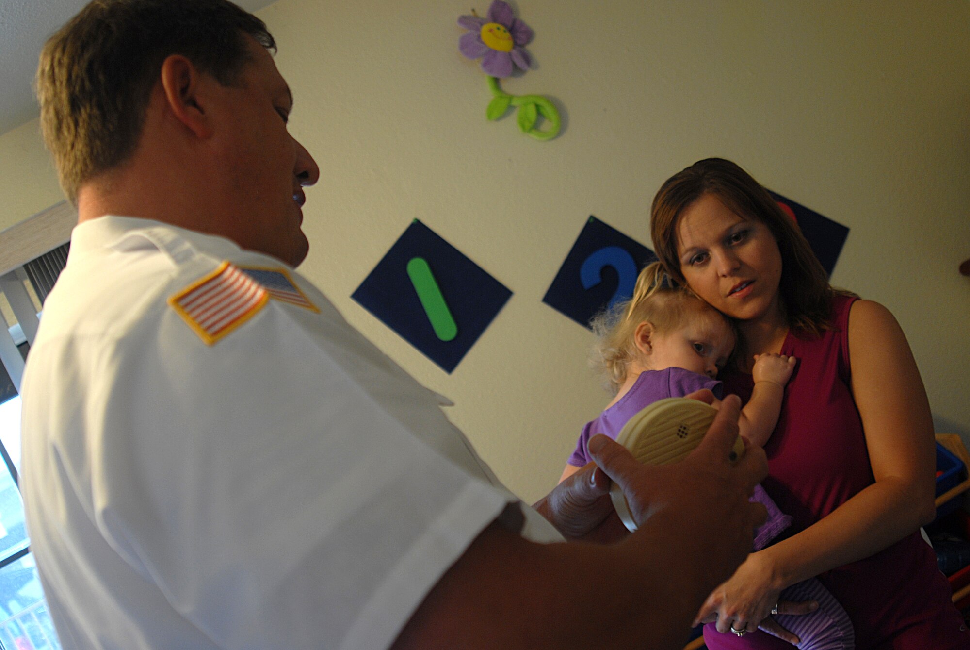 GOODFELLOW AIR FORCE BASE, Texas -- Assistant Fire Chief for Prevention, Glenn Haffner, 17th Civil Engineer Squadron, explains to Crystal McMichael how to check and change smoke alarm batteries in base housing, as Kaedyn, 22 months, looks on Sept. 24. The Goodfellow Fire Emergency Services will be out and about to spread the word on fire prevention and life safety. (U.S. Air Force photo/ Senior Airman Tong Duong)