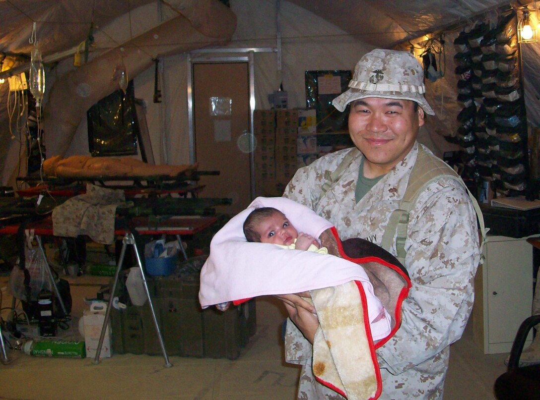 Lt. Cmdr. Stephen Tantama, Emergency Medicine Physician, Charlie Surgical Company, 1st Medical Battalion, Combat Logistics Regiment 15 (Forward), 1st Marine Logistics Group (FWD) holds the Afghan baby whose life was saved by him and his team.