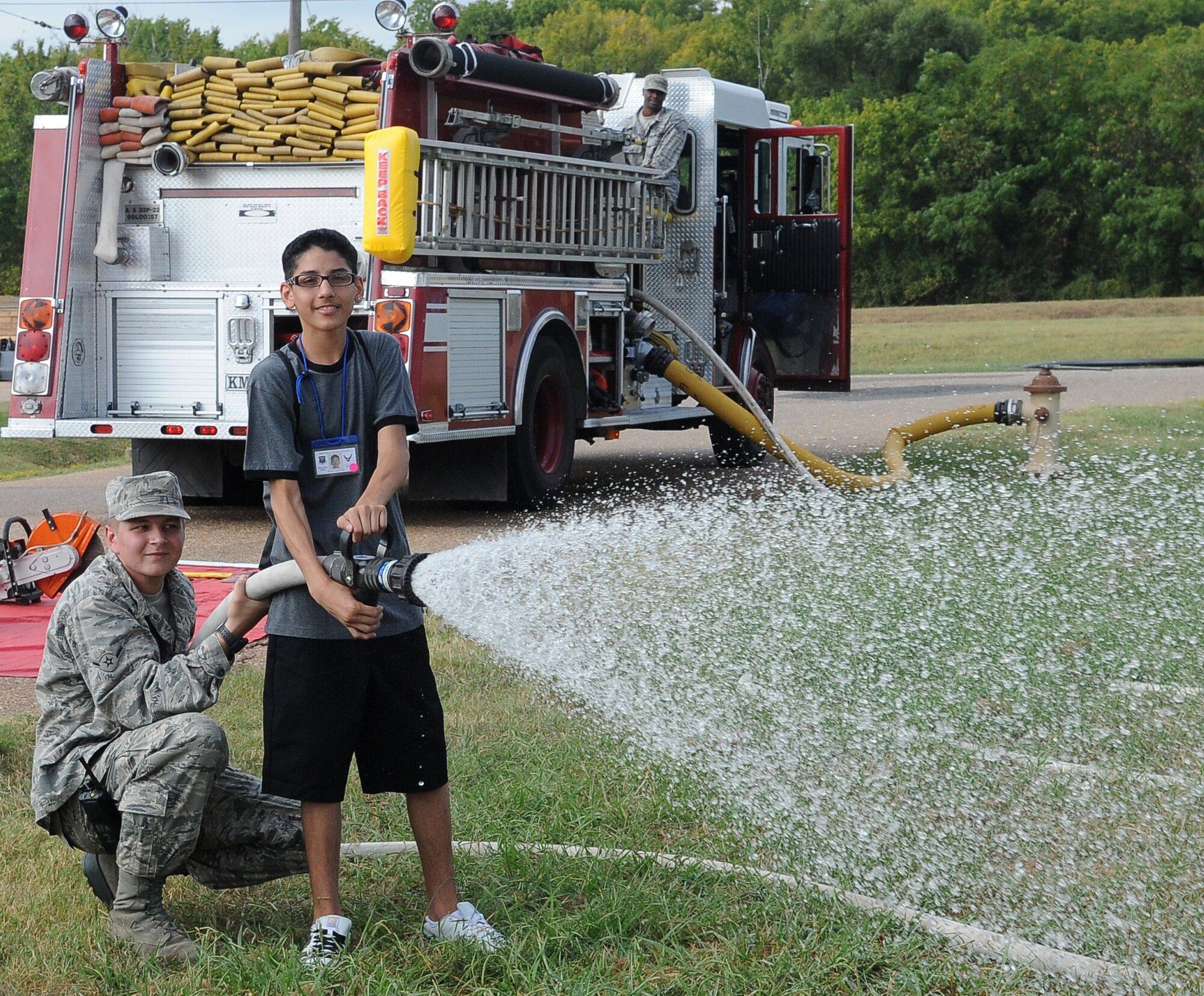 BARKSDALE AIR FORCE BASE, La. -- Airman Michael Scheid, 2nd Civil Engineer squadron, assists a child in using the fire hose during Operation Hero, Sept. 25. More than 130 children and 90 parents participated in the mock-deployment line to help children understand what their military parents experience before deploying downrange. Some activities included a weapons qualification with paintball guns, chemical readiness preparation and a physical fitness assessment. (U.S. Air Force photo/Senior Airman Amber Ashcraft) (RELEASED)