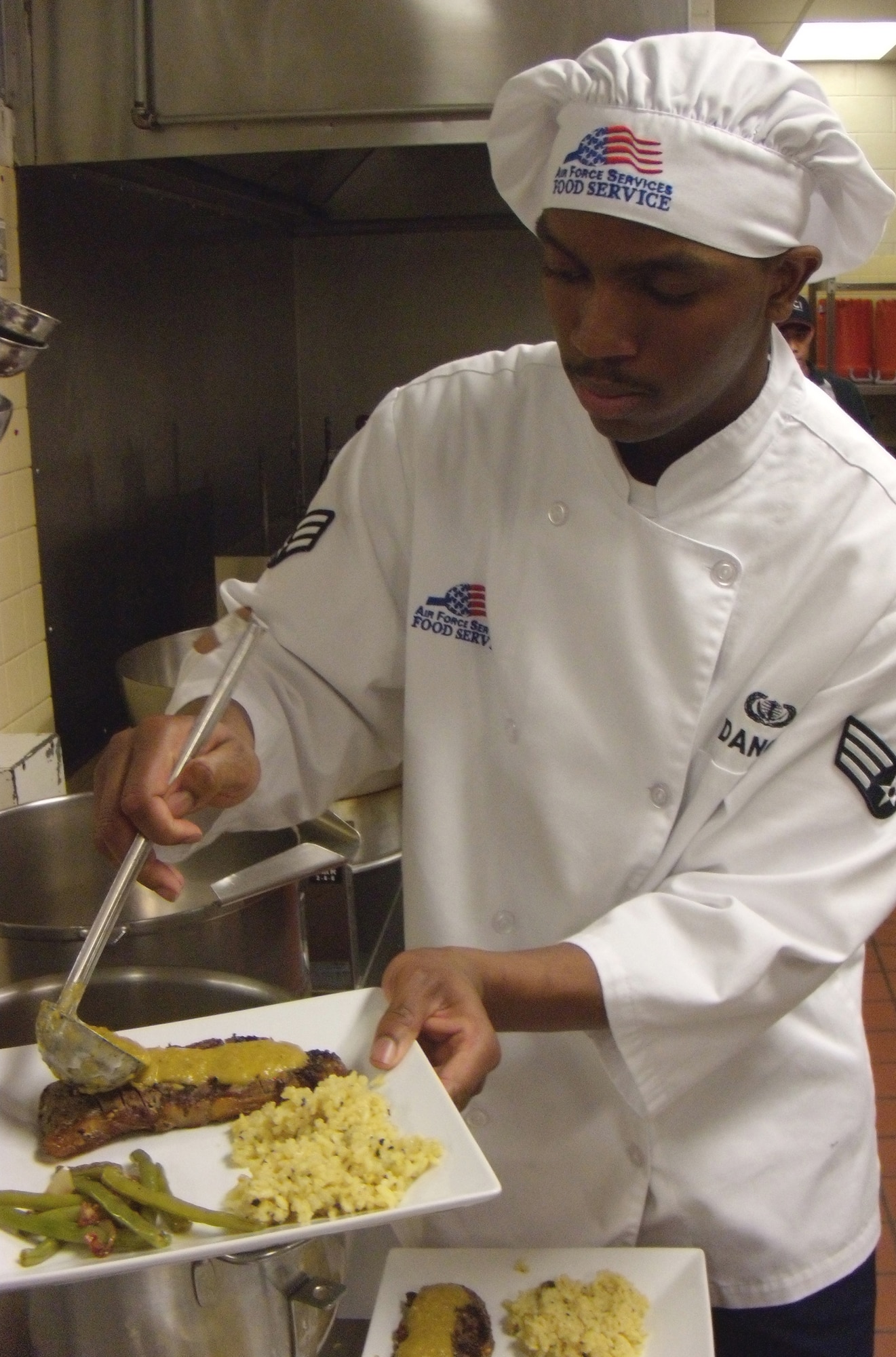 Senior Airman Timothy Dance, 436th Force Support Squadron Head Chef, pours a glaze on to a Bistecca con Pomodori alla Griglia, a pepper-crusted steak topped with grilled seasoned tomatoes and peppers, served with risotto and green beans, for a Patterson Dining Facility Birthday Meal, Sept. 23, 2010, at Dover Air Force Base, Del. (U.S. Air Force photo by Senior Airman Shen-Chia Chu/Released)