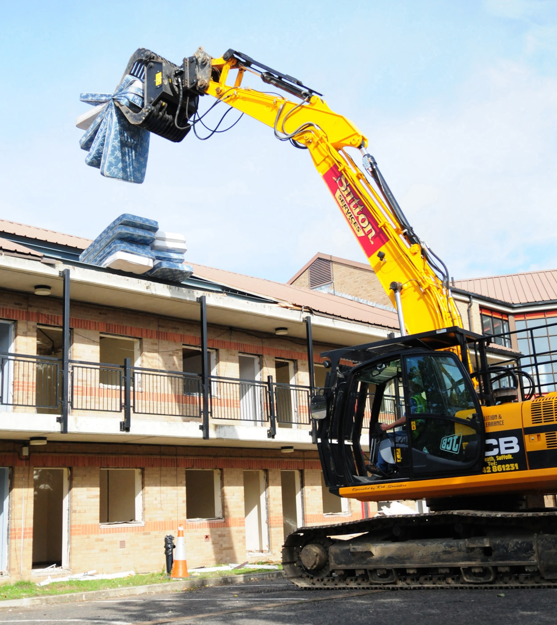 RAF MILDENHALL, England -- A dinosaur-like JCB picks up old mattresses ready to drop them in the dumpster in preparation of demolition of old dormitories here. Contractors are clearing Dorm 212 before it's knocked down. The quality of the Airmen's quarters had deteriorated and had become surplus to requirements. Once demolition is complete, which is scheduled for January 2011, the area will be landscaped. (U.S. Air Force photo/Karen Abeyasekere)