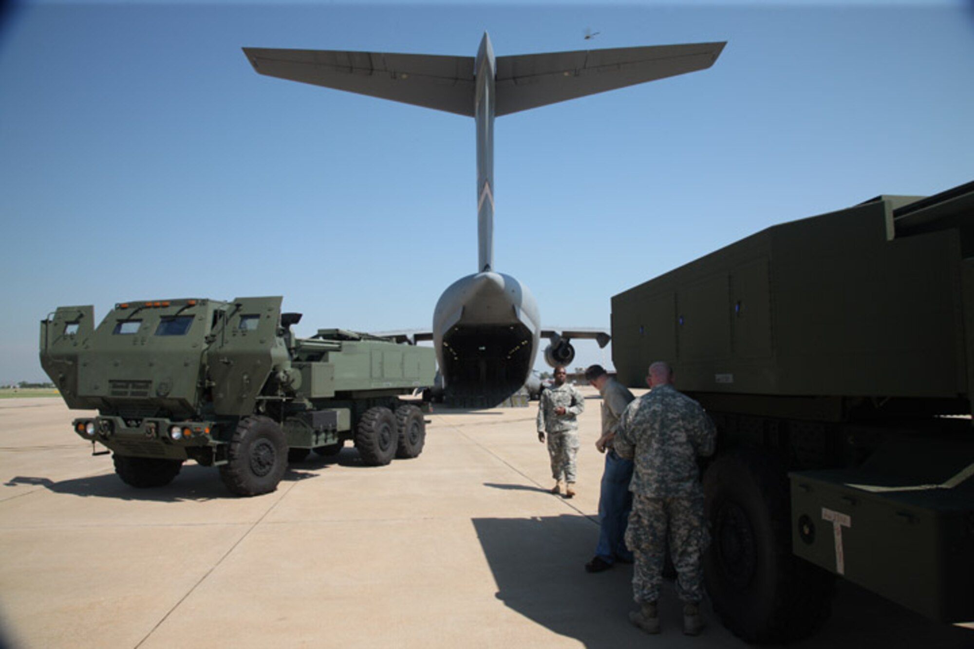 The tail of an Altus AFB C-17 "Globemaster III" stands high in the air overlooking two High Mobility Artillery Rocket Systems at Lawton-Fort Sill Regional Airport Sept. 16. A group from Product Manager Field Artillery Launchers, Precision Fires Rocket and Missiles Systems, Fort Sill Master Gunners Division, Lockheed Martin, and L-3 Communications loaded the launchers on the aircraft to test an upgrade to the Universal Fire Control Systems on the HIMARS. The upgrade, called "Hot Panel" is meant to allow the fire control system to track the HIMARS global position while it's transported in flight. (U.S. Army photo by Marie Berberea)