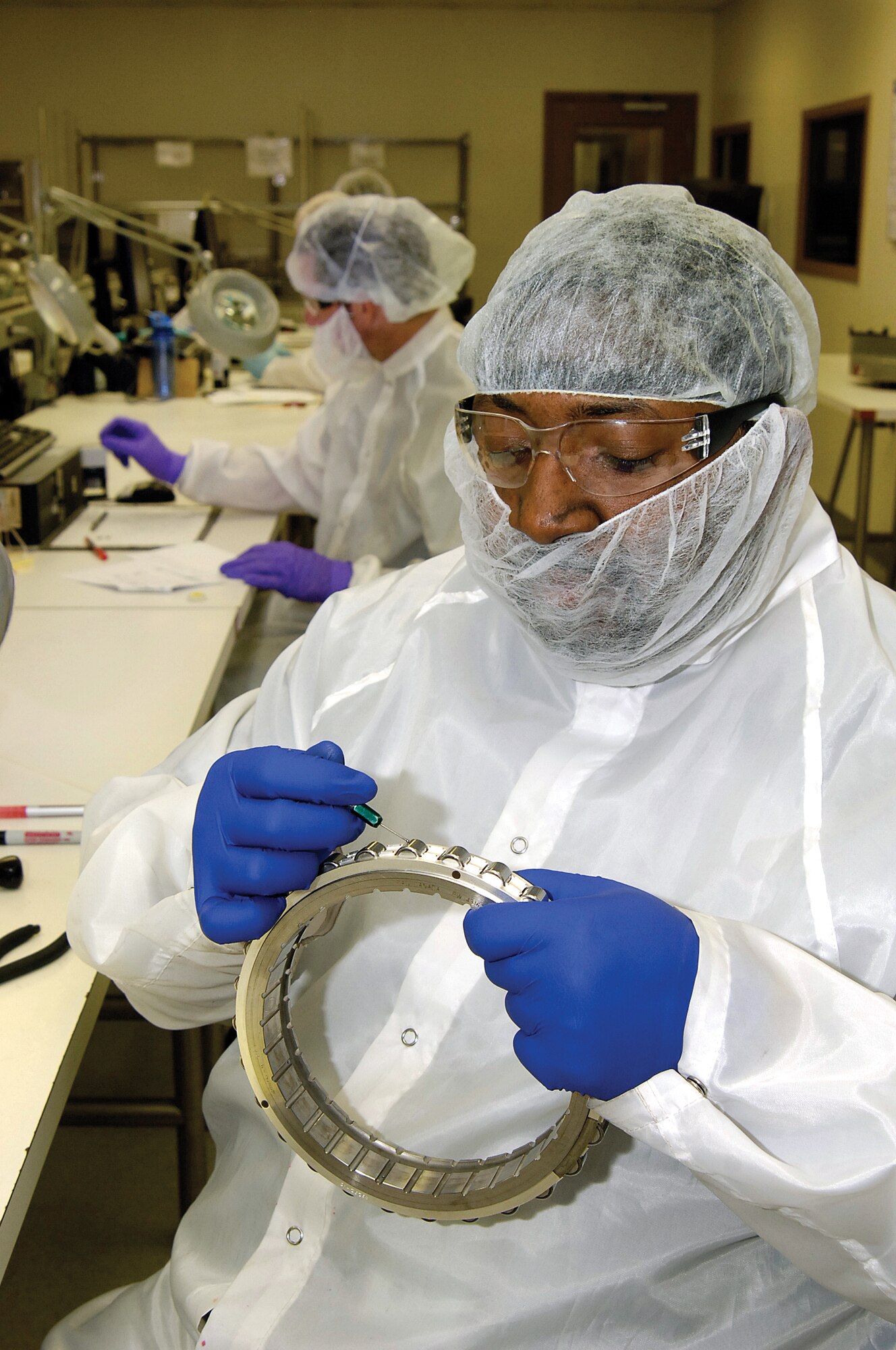 Covered to protect bearings from contaminants in the Bearing Overhaul Shop’s clean room, Kevin Ward checks an F119 inner race bearing for damage, rust or other imperfections.  Mr. Ward runs a ball scribe over the surface and feels any pitting or areas that need further inspection.  Working behind Mr. Ward is Richard Moio.  (Air Force photo by Margo Wright)