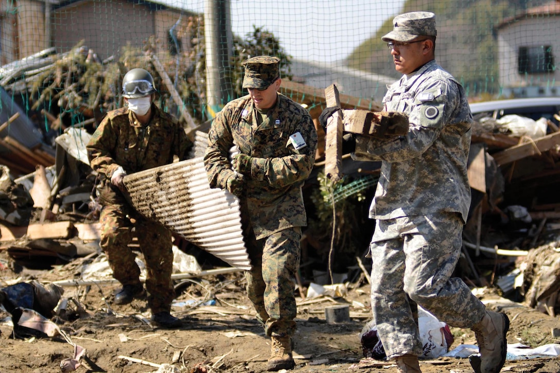 Army Sgt. Joel Rodriguez, right, generator technician, and Capt. Adan Maldonado, middle, liaison officer to Japan Ground Self-Defense Force 5th Brigade, both with Joint Support Force Japan, work with a JGSDF member to move debris in Ishinomaki, Japan, April 1. The Logistics Combat Element, 3rd Marine Expeditionary Brigade (Forward), led the U.S. forces participating in the cleanup which focused on preparing the school to reopen in the coming months.
