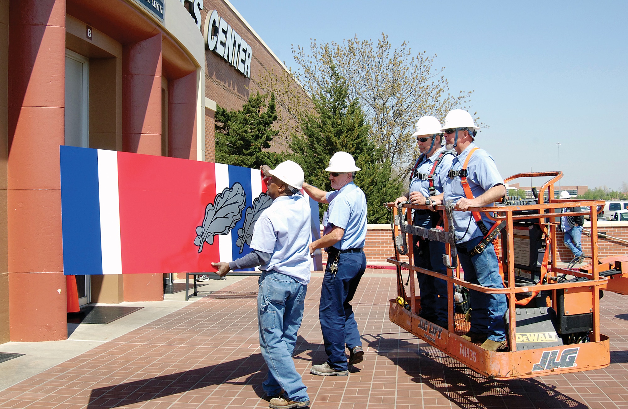 Workers prepare to install a new Air Force Organizational Excellence Award ribbon above the doors at Bldg. 3001, the Oklahoma City Air Logistics Center headquarters. The sign features a  new silver oak leaf cluster, signifying the 11th time the center has received the award. (Air Force photo by Margo Wright)