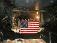 Crew members from the 337th Airlift Squadron hold up an 8' by 12' flag on the ground at a runway in Afghanistan.  They will donate the flag to Plymouth, Mass., parade officials for use in their 2011 America's Hometown Thanksgiving Celebration.
In November, parade director Olly Machado donated their U.S. flag to the Air Force performance band, Tops in Blue, to bring with them to Afghanistan and present to the troops during their Christmas tour. 
That left the committee without a flag, so flight engineer Master Sgt. Eric McGlynn and his wife purchased a replacement flag, which Sergeant McGlynn brought downrange.

       