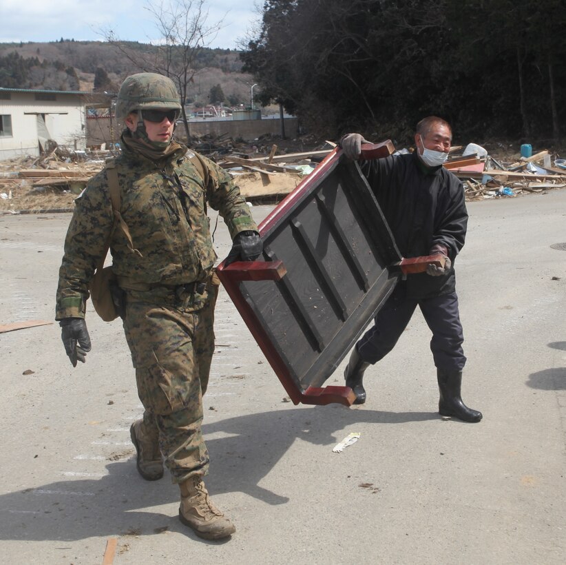 A Marine with Battalion Landing Team, 2d Battalion, 5th Marines, 31st Marine Expeditionary Unit, helps a local man remove an unscathed table from a severely damaged house here during Operation Field Day, a debris-clearing and cleanup project designed to open harbor access and area roads on the isolated island.  As Marines cleared the area, they took time to locate personal items which could be salvaged by the local residents.  The 31st MEU is participating in Operation Tomodachi at the request of the Japanese government after the 9.0 earthquake and tsunami devastated the northeast coast of Japan.