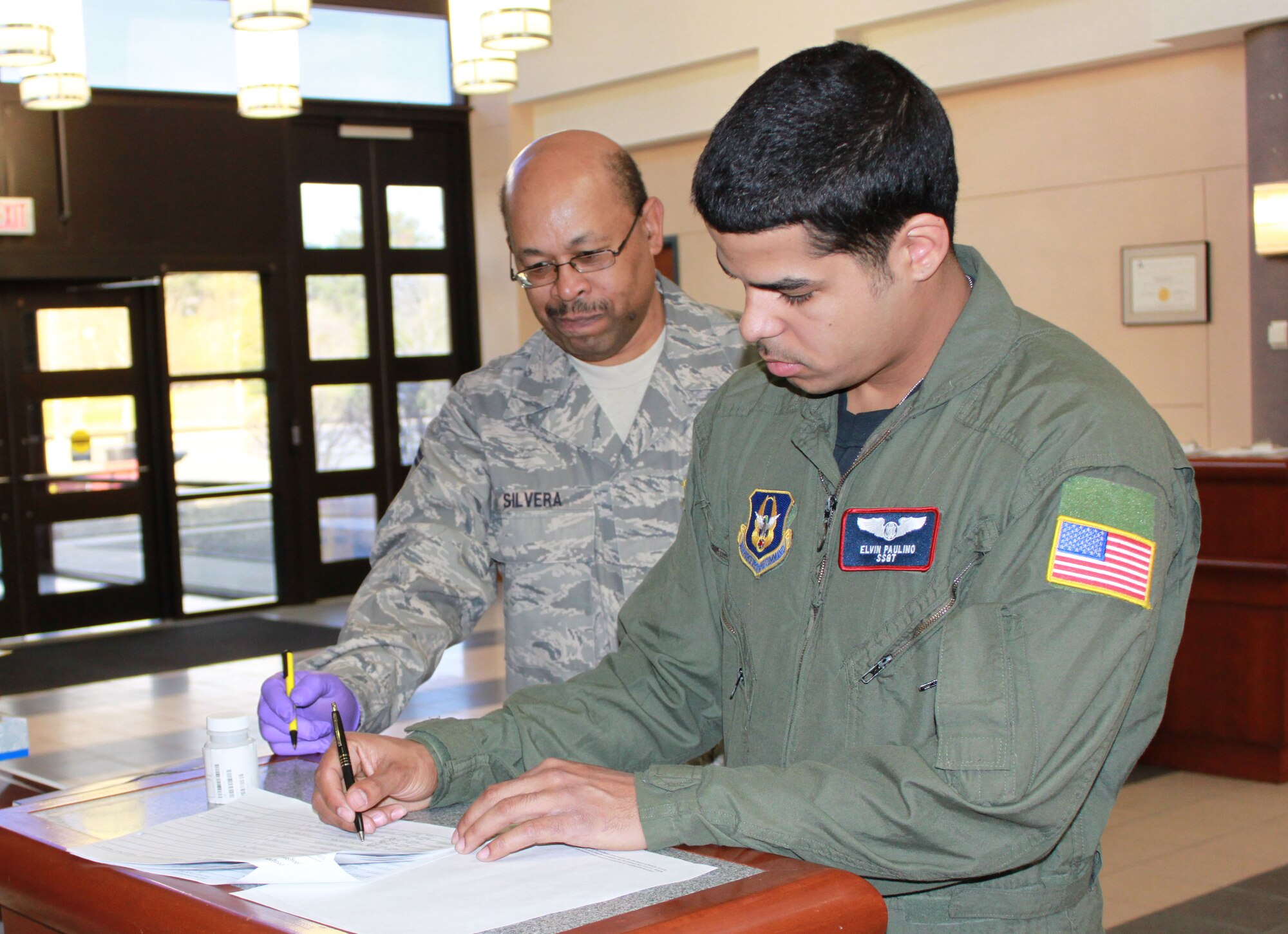 JOINT BASE MCGUIRE-DIX-LAKEHURST, N.J. - 514th Air Mobility Wing member and observer for the day, SMSgt Osmond Silvera, looks on as fellow member, SSgt Elvin Paulino receives a specimen bottle for urinalysis. Observers ensure proper procedures are followed throughout a urinalysis test. Air Force Reserve Command implemented a new instruction for urinalysis that randomly selects 25 percent of members per month for testing, up from 2 percent with the old policy. Some members may be selected more than once in a given period, while others not at all. (U.S. Air Force photo/Staff Sgt. Monica Dalberg)