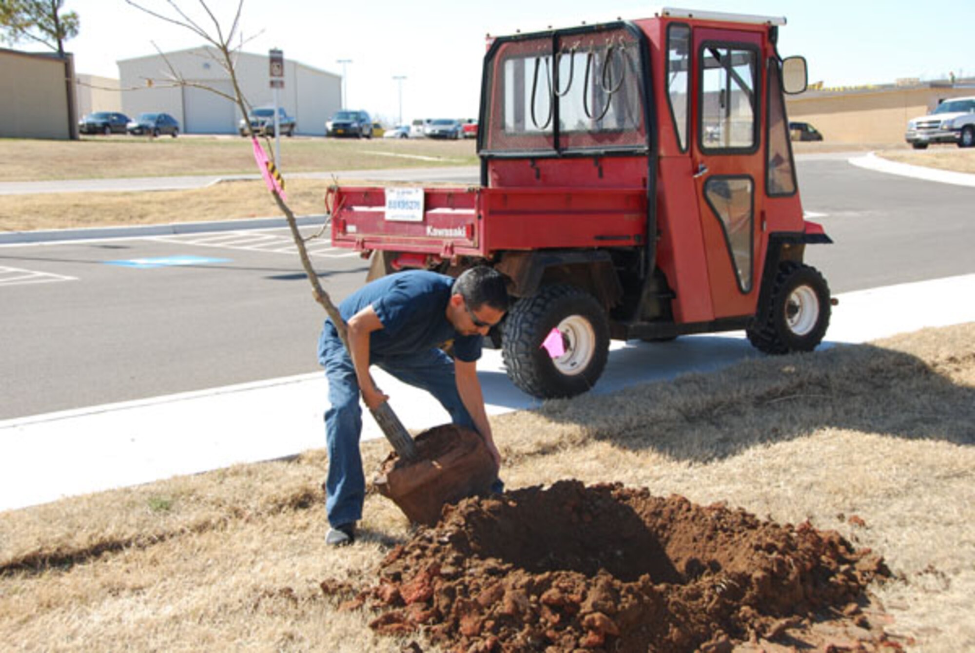 A volunteer picks up a tree to plant in a freshly dug hole. The tree planting project involved 59 trees, more than 25 volunteers, two hours and one sunny afternoon to beautify the exterior of the Reserve-Guard operations building on the reserve camputs of Tinker Air Force Base on March 10, 2011.