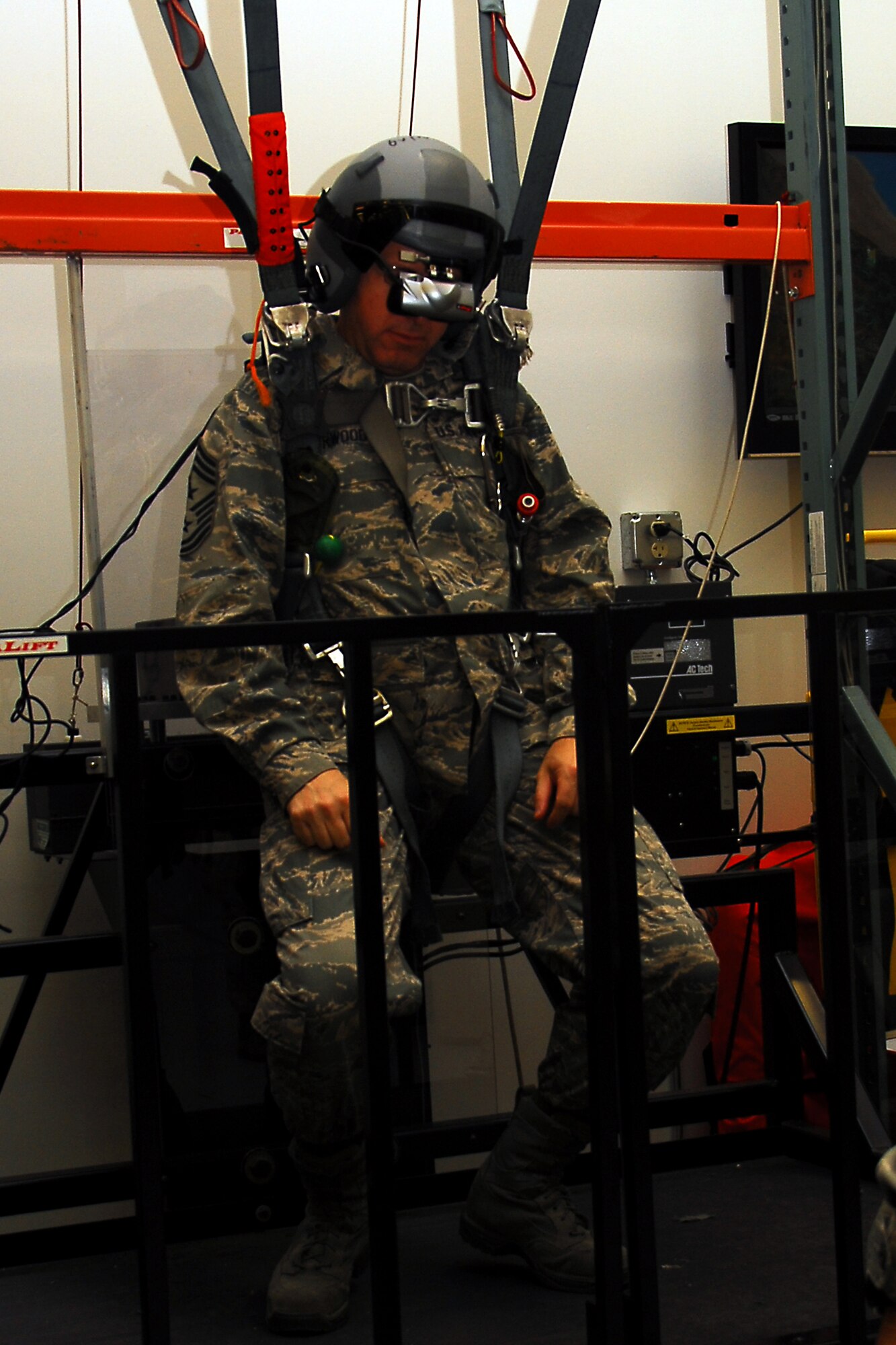 Chief Master Sergeant Steven Larwood, 22nd Air Force command cheif, sits in the horness of a parachute simulator in the 403rd Aircrew Flight Equipment shop. Master Sergeant Ray Reynolds, 403rd AFE supervisor, instructs the chief on how to operate the simulator when he stop to visit the shop as part his visit to the 403rd Wing. (U.S. Air Force Photo by Senior Airman Tabitha Dupas)