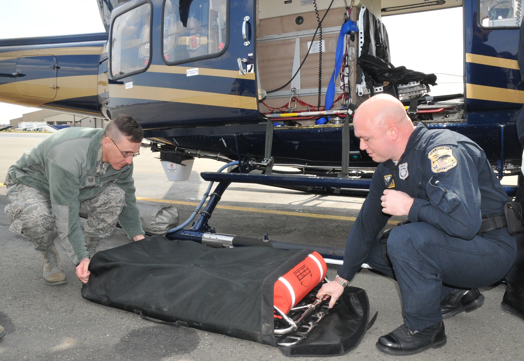 Tech. Sgt. Robert Burns, a reservist with the 512th Aerospace Medicine Squadron, assists Cpl. Jason Baxley, a medic with the Delaware State Police Aviation Section, in setting up a hoist. This device is attached to a cable and used to raise or lower goods or personnel. The 512th AMDS paired up with the DSP to get helicopter familiarization training and learn how DSP emergency responders conduct their mission. (U.S. Air Force photo by Capt. Marnee A.C. Losurdo)