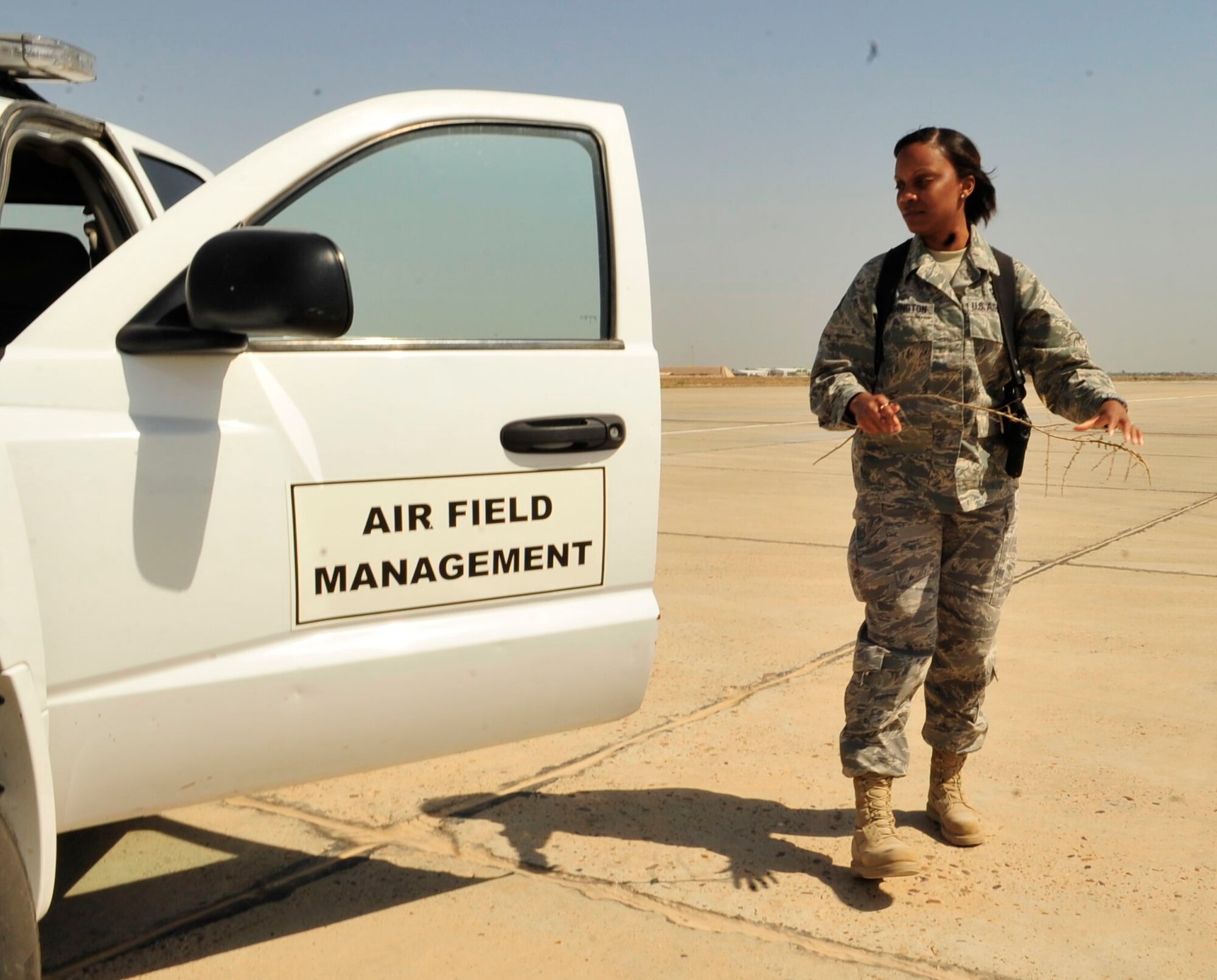 U.S. Air Force Staff Sgt. Carla Washington, airfield management operations NCO-in-charge, 447th Expeditionary Operations Support Squadron, Sather Air Base, Iraq, March 31, 2011, picks up foreign object debris, in this instance, part of a plant, and removes it from the flight line. FOD can cause serious damage to aircraft engines. (U.S. Air Force photo by Senior Master Sgt. Larry Schneck/Released)