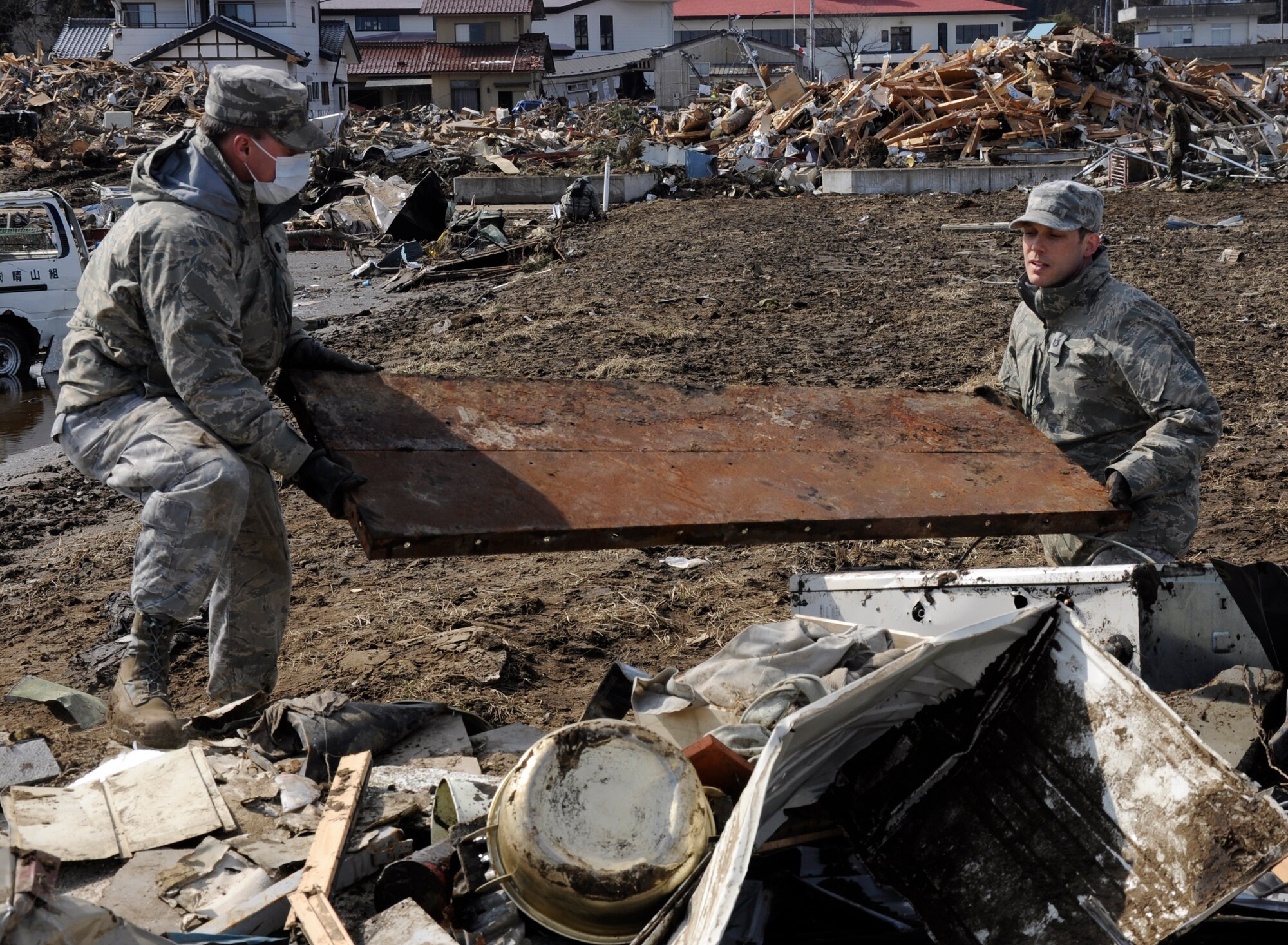 NODA MURA, Iwate, Japan – Lt. Col. Eric Winton, 373rd Intelligence Group, left, and Tech. Sgt. Gregory Bird, 35th Maintenance Group, right, carry debris across a tsunami-struck area here March 29. Both Airmen are assigned to Misawa Air Base, Japan, and were among nearly 40 U.S. service members and civilians who left the base to assist in tsunami cleanup and relief efforts in the village as part of Operation Tomodachi. (U.S. Air Force photo by Senior Airman Joe McFadden/Released)