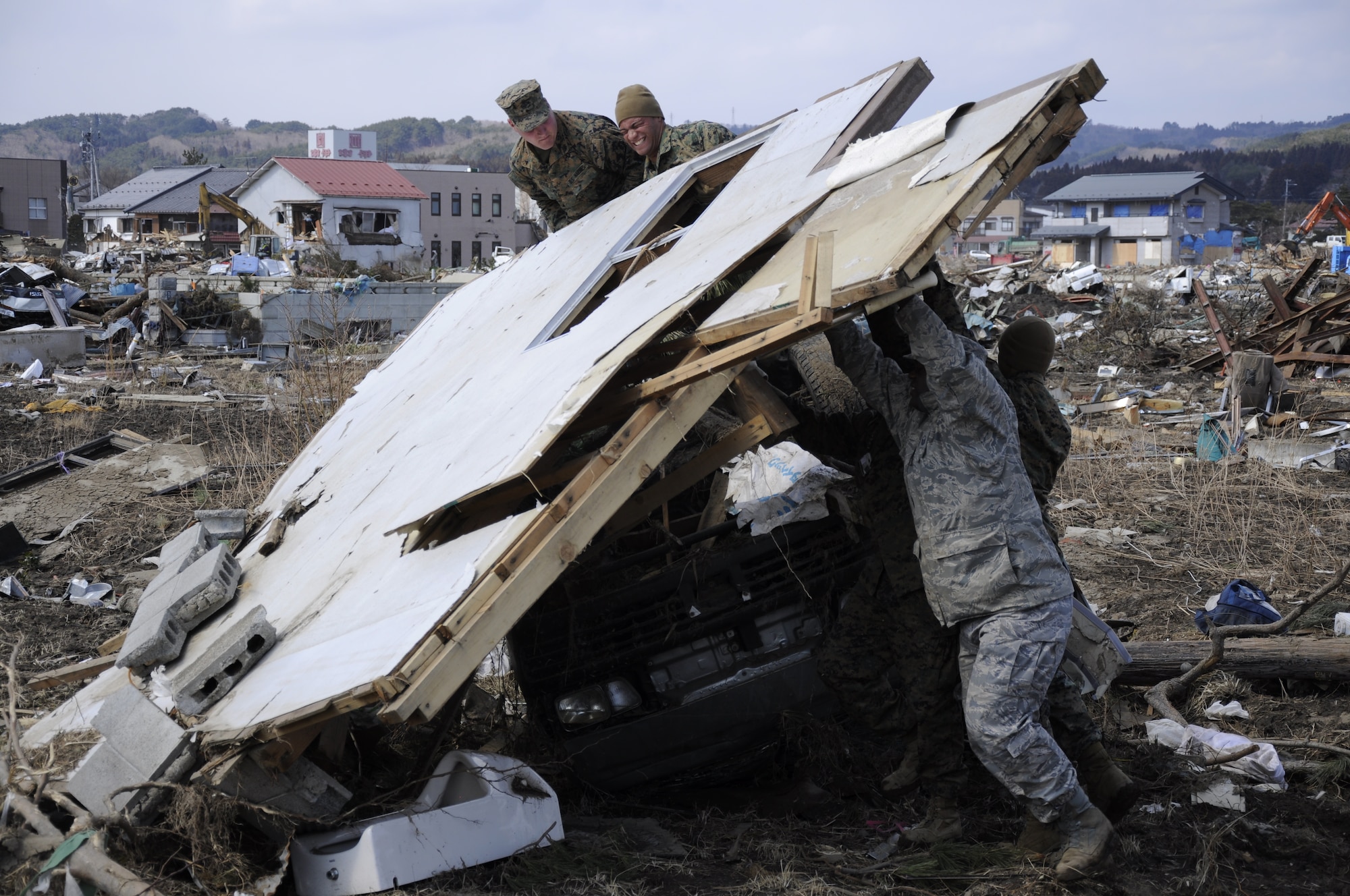 NODA MURA, Iwate, Japan – U.S. service members lift a knocked-down wall off a damaged car in a tsunami-struck area here March 29. Nearly 40 U.S. service members and civilians left Misawa Air Base, Japan, to assist in tsunami cleanup and relief efforts in the village as part of Operation Tomodachi. (U.S. Air Force photo by Senior Airman Joe McFadden/Released)