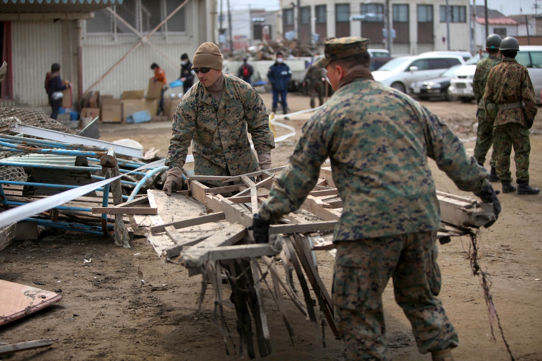 U.S. Marine Corps Staff Sgt. German Estrada, left, and Staff Sgt. Jaime Barajasmora carry a piece of debris while helping to clean the Minato Elementary School in Ishinomaki, Aichi, Japan. April 2, 2011. Estrada and Barajasmora are assigned to the 3rd Marine Expeditionary Brigade. Marines and members of the Japan Self-Defense Force helped clean debris from the school as part of Operation Tomodachi.