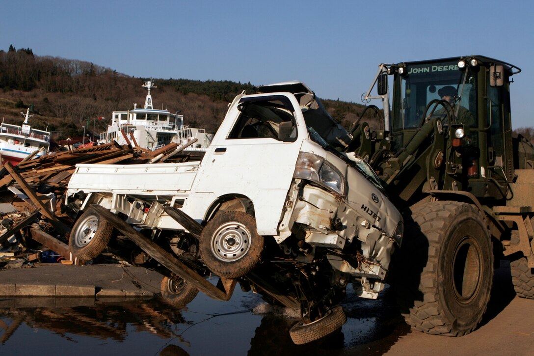 Heavy equipment operated by a Marine with the 31st Marine Expeditionary Unit, carries a destroyed truck to a collection point, where over 100 others rest. As part of Operation Tomodachi, the 31st MEU is ready to support our Japanese partners and to provide assistance when called upon.