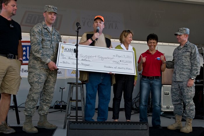 NELLIS AIR FORCE BASE, Nev. -- Col. Steven Garland 99th Air Base Wing commander, accepts a $10,000.00 check from Bill Mayne, Academy Country Music chairman and Sarah Trahern, Academy of Country Music president, for Nellis youth programs April 2. Country music stars came to Nellis to participate in a charity skeet shooting event and perform a free concert for military members and their families. ( U.S Air Force Photo by Airman 1st Class Daniel Hughes)