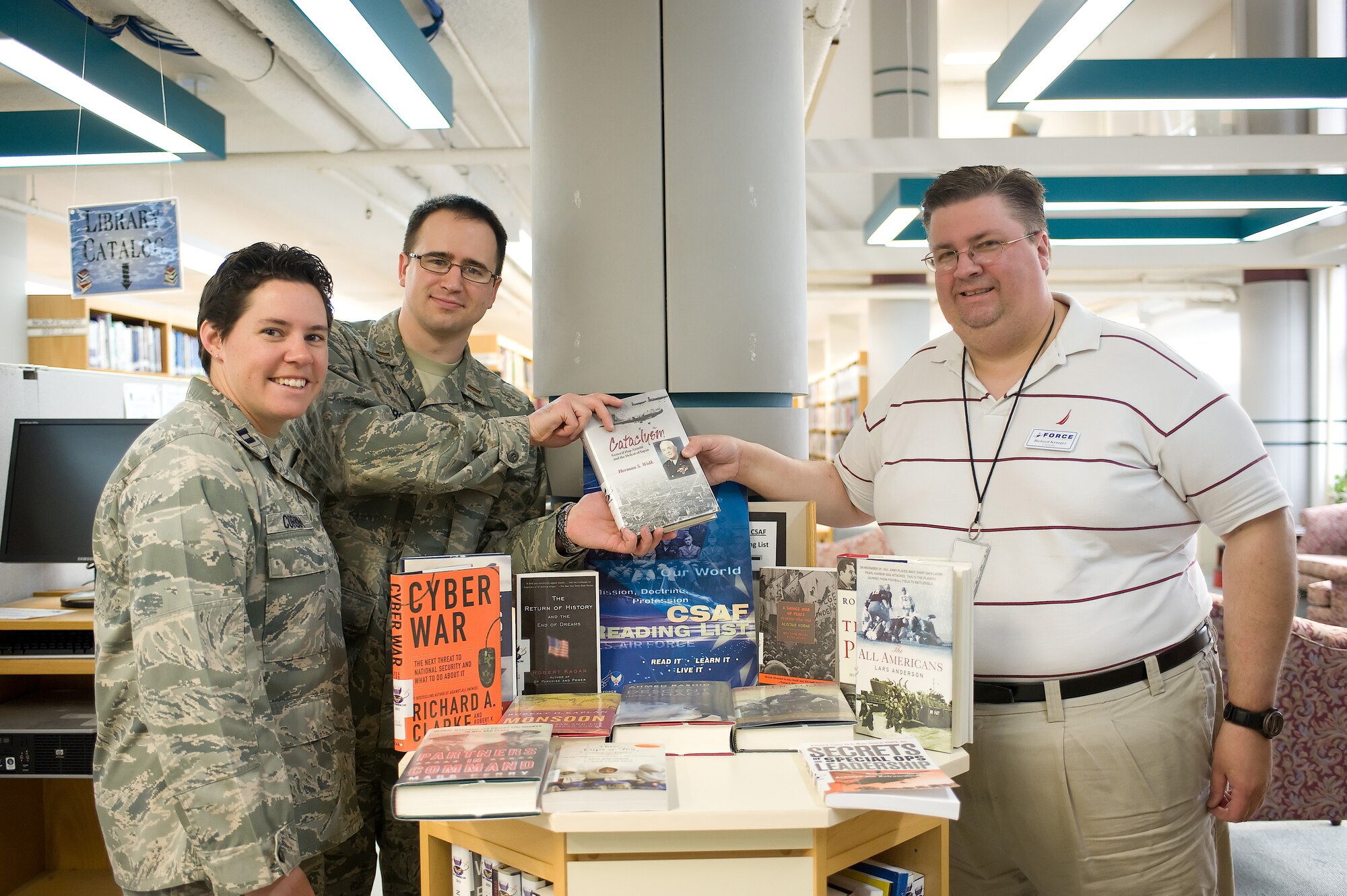 Capt. Rebecca Corbin (left) and 2nd Lt. Hans Hobbs, representing company grade officers who donated the entire Chief of Staff of the Air Force's Reading List, stand with Richard Krueger, base librarian, April 5, 2011, at Dover Air Force Base, Del.'s library. The books were donated in honor of CGOs who have died in support of Operation Enduring Freedom and Operation Iraqi Freedom. Each book's inside cover has an information vignette of a fallen CGO. (U.S. Air Force photo by Steve Kotecki)