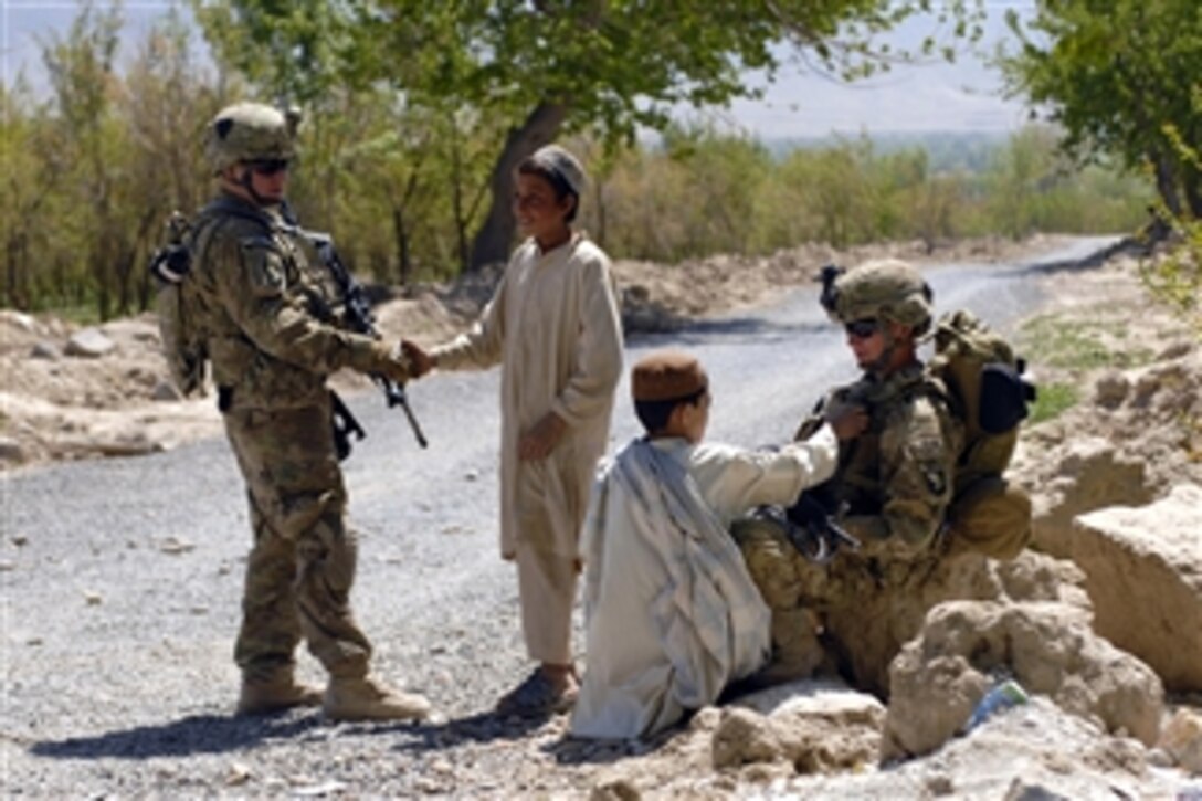 U.S. Army Cpl. Anthony Gomez (left) shakes the hand of a young resident of Tarok Kolache while Pfc. Roy Heggernes (right) interacts with a young boy during a ribbon cutting ceremony for a new village mosque in Kandahar Province, Afghanistan, on April 1, 2011.  