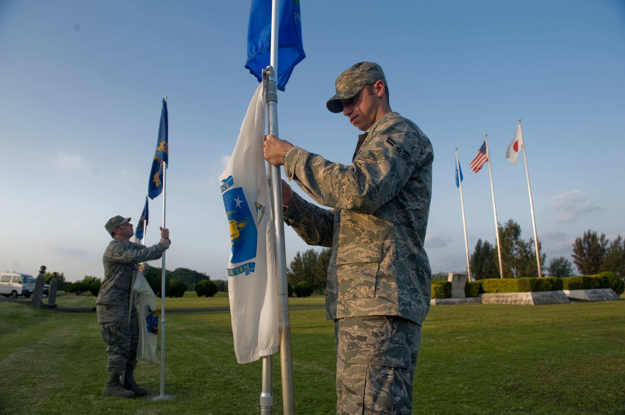 KADENA AIR BASE, Japan - Airman 1st Class Daniel Davis, 18th Component Maintenance Squadron, and Airman 1st Class Jordan Arnold, 353rd Special Operations Group, raise state flags at 18th Wing headquarters April 5. Airmen Davis and Arnold are part of the Kadena Pride Team responsible for cleaning up the base. (U.S. Air photo/ Staff Sgt. Jonathan Steffen)