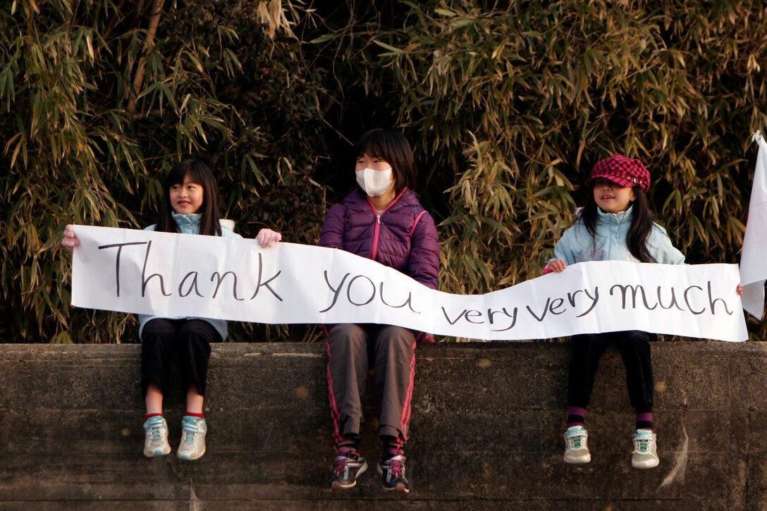 Two children hold a banner with their mother, thanking Marines and Sailors of the 31st Marine Expeditionary Unit for their work, April 7. The Marines and Sailors spent about six days cleaning up debris on parts of the island, during Operation Field Day. The 31st MEU's involvement is part of the larger Operation Tomodachi, coordinated after a 9.0 earthquake and subsequent tsunami struck Japan causing widespread damage. The 31st MEU remains ready to support its Japanese partners and to provide assistance when called upon.