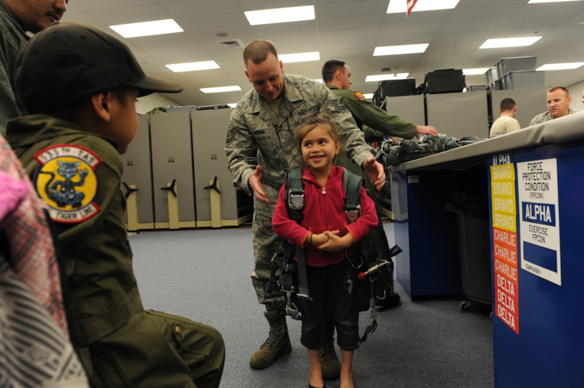 Seven year-old Jonah "J-Boy" Kalaikai watches as his six year-old sister is thrilled to put on a flight harness with the help of Technical Sergeant Bobby Pickel while at the 535th Airlift Squadron, Joint Base Pearl Harbor-Hickam (JBPHH), Hawaii on April 2, 2010. J-Boy was invited to JBPHH to participate in the "Pilot for a Day" program which is a partnership between Kapi'olani Medical Center and the 15th Airlift Wing that gives a special day to a child that is dealing with a serious or chronic condition. Jonah was diagnosed with Acute Myeloid Leukemia at age two and has been in and out of remission five times since then. (U.S. Air Force photo/Tech Sgt. Cohen A. Young)