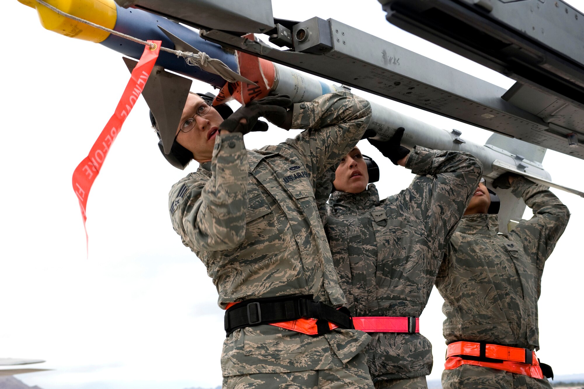 NELLIS AIR FORCE BASE, Nev.-- Senior Airman Lucas Wolf, Airman 1st Class Amanda Schreckengost, load crew members, and Staff Sgt Jason Spears, weapons load crew chief, 57th Aircraft Maintenance Squadron, load an Air Intercept Missile- 9M Sidewinder onto an F-16 during the 1st quarterly weapons load competition April 8. Weapons load competitions are conducted quarterly to keep Airmen sharp and recognize superior performers. Weapons load teams are evaluated for their use of the checklist, safety, and overall speed. (U.S. Air Force photo by Airman 1st Class Matthew Lancaster)
