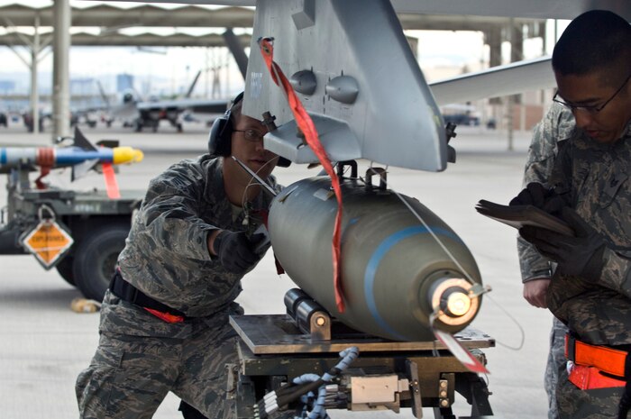 NELLIS AIR FORCE BASE, Nev.-- Senior Airman Lucas Wolf, 57th Aircraft Maintenance Squadron, load crew member, loads a Mark-82 bomb onto an F-16 while Staff Sgt. Jason Spears, weapons load crew chief, does the loading checklist during the 1st quarterly weapons load competition April 8.  Weapons load competitions are conducted quarterly to keep Airmen sharp and recognize superior performers. Weapons load teams are evaluated for their use of the checklist, safety, and overall speed. (U.S. Air Force photo by Airman 1st Class Matthew Lancaster)
