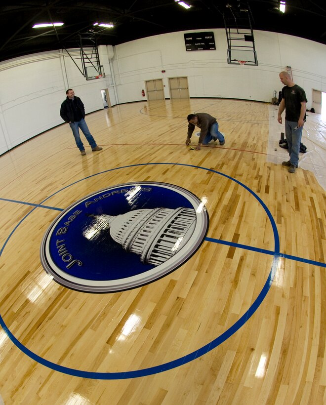 The West Fitness Center will sport a new Joint Base Andrews logo at center court, in between an 11th Wing logo and U.S. Navy logo. The newly installed basketball court will serve dually as a volleyball court for the upcoming Joint Andrews Base intramural sports season. The project is scheduled for completion by April 29. (Photo by Bobby Jones) 